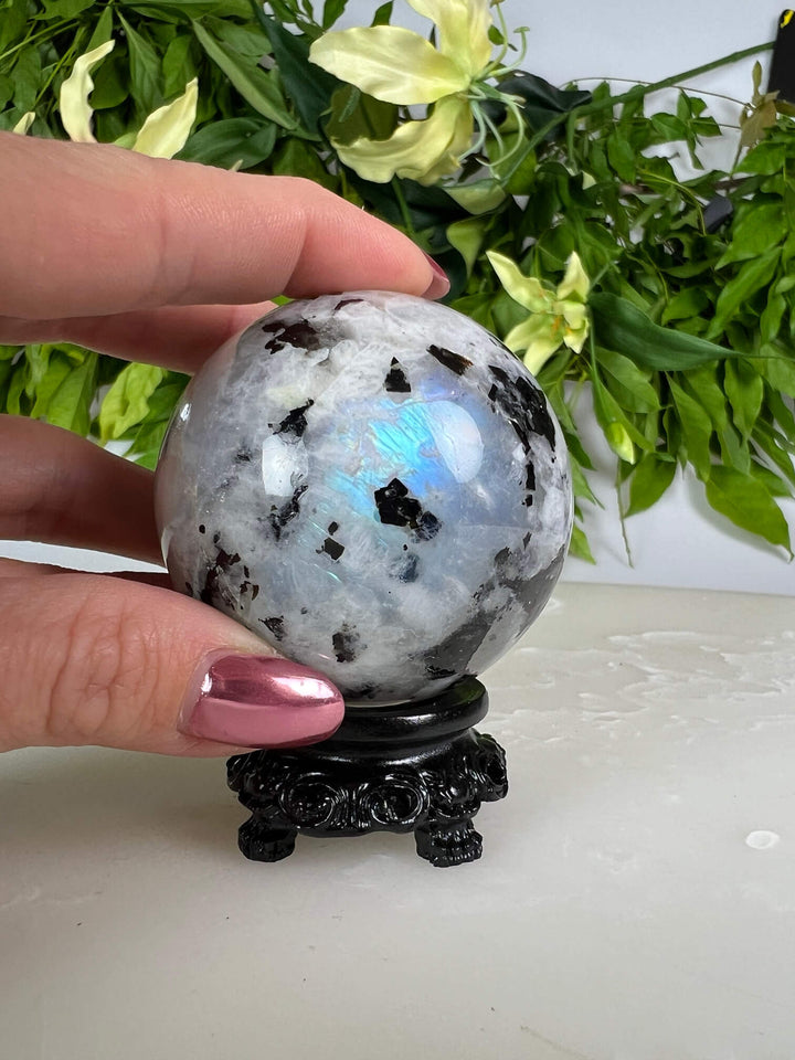 Maansteen bol 1 met blauwe flash op zwarte bolhouder design met pootjes en met hand.