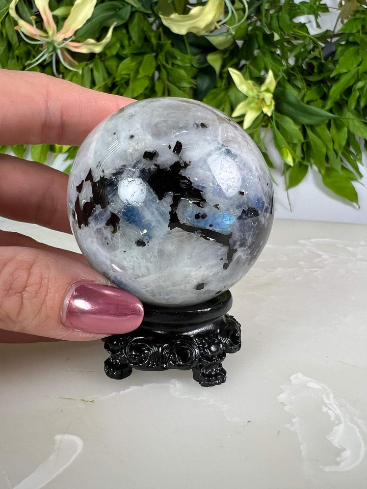 Maansteen bol 2 met blauwe flash op zwarte bolhouder design met pootjes  en met hand.