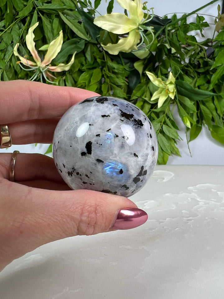 Maansteen bol 3 met blauwe flash op zwarte bolhouder design met pootjes  en met hand.