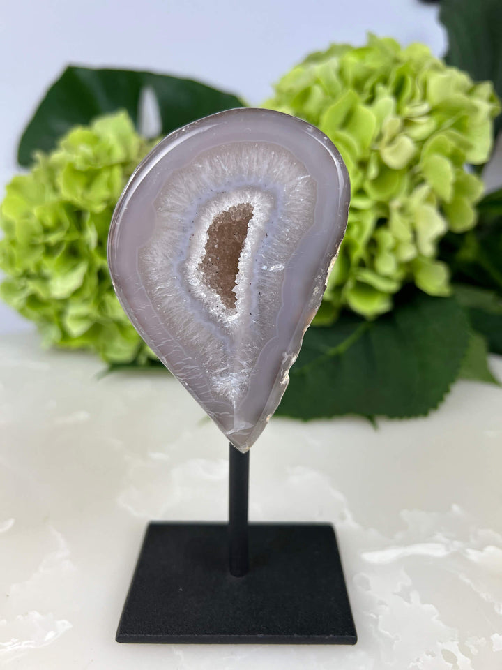 Voorkant van de agaat geode met fijne kristallen op zwarte standaard.