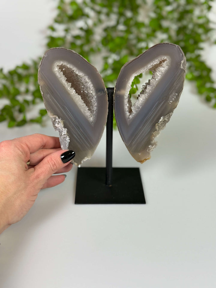 Voorkant van de agaat vlinder in lichte kleur op zwarte standaard met hand. Met kleine kristalpuntjes. Rechter vleugel met een portal.