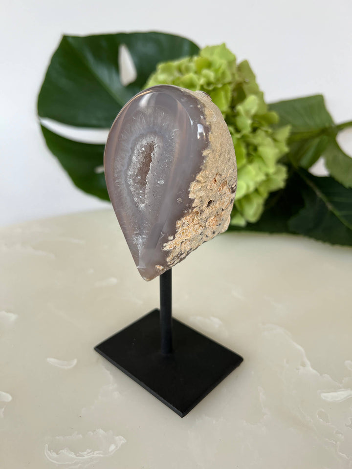 Zijkant van de agaat geode met fijne kristallen op zwarte standaard.